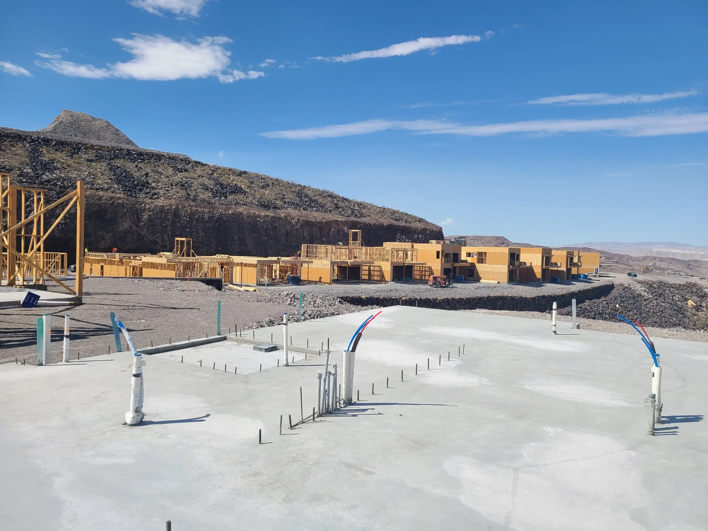 Construction site with concrete foundation and stacked wooden frames under a blue sky.